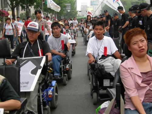 고인들의 영정을 들고 빨간 리본을 단 장애인들이 광화문까지 행진하고 있다. ⓒ2006 welfarenews