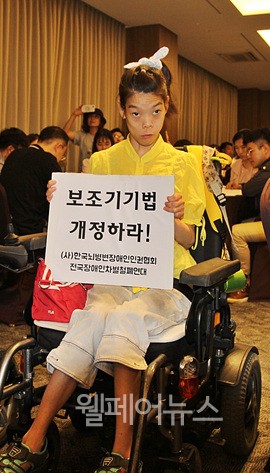 ▲ 장애인 활동가가 ‘보조기기법 개정하라’는 손팻말을 들고 있다.