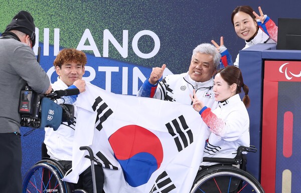 택극기를 들고 있는 백혜진 이용석 선수는 태극기를 들고 있으며, 감독과 코치는 엄지척을 하고 있다.